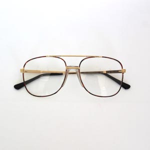 May include: Aviator-style eyeglasses with a gold-tone metal frame and clear lenses. The frames have a brown tortoiseshell pattern around the lenses and black temples. The glasses have a double bridge design.