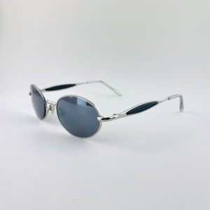 May include: Silver oval-shaped sunglasses with black accents on the arms. The lenses are dark grey.