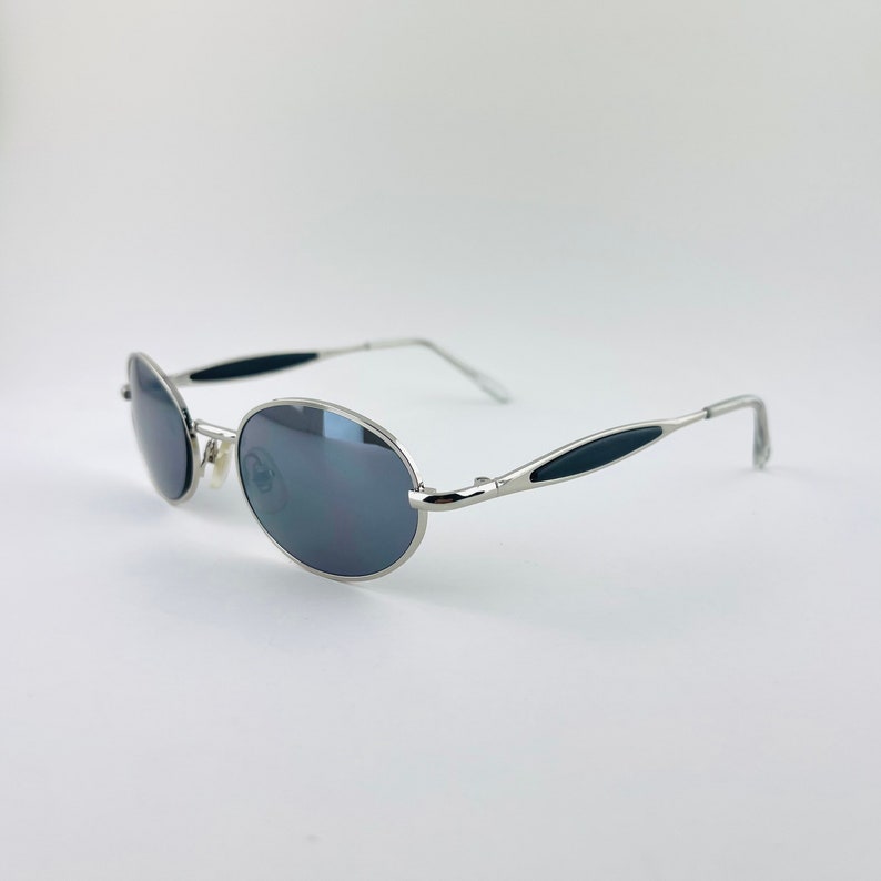 May include: Silver oval-shaped sunglasses with black accents on the arms. The lenses are dark grey.