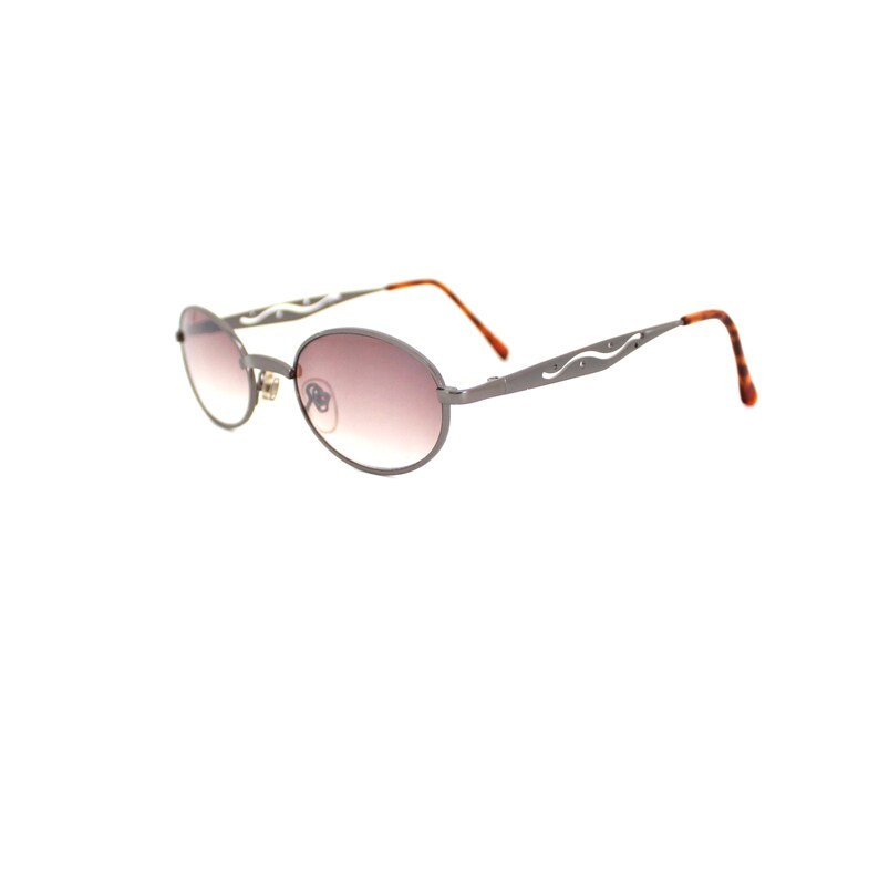 Pode incluir: Um par de &oacute;culos de sol ovais com arma&ccedil;&atilde;o de metal prateado e lentes marrons. A arma&ccedil;&atilde;o tem um design decorativo nas hastes.