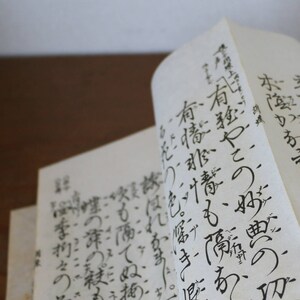 Könnte beinhalten: Nahaufnahme eines Buches mit handschriftlichem japanischem Text. Die Seiten sind geöffnet und der Text ist sichtbar. Das Buch liegt auf einer Holzoberfläche.