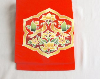 May include: A red fabric panel with a gold and green floral design featuring two birds. The design is centered on the panel and has a symmetrical pattern.