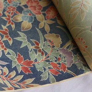 May include: A roll of fabric with a floral pattern in shades of red, blue, green, and yellow on a navy blue background. The fabric has a subtle textured pattern.