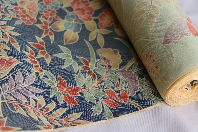 May include: A roll of fabric with a floral pattern in shades of red, blue, green, and yellow on a navy blue background. The fabric has a subtle textured pattern.
