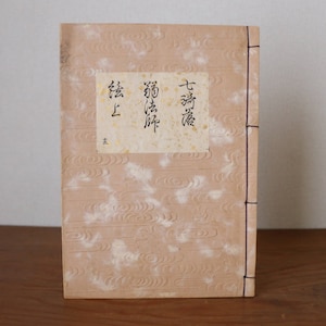 Könnte beinhalten: Ein beigefarbenes Buch mit einem strukturierten Einband und einem weißen Etikett mit japanischem Text, der "上巻", "新編" und "都府楼" lautet, was mit "Band 1", "Neuauflage" und "Tofu-Schloss" übersetzt wird.