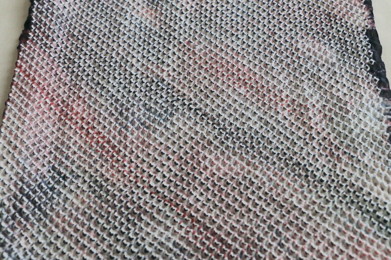 May include: Close-up of a woven fabric with a textured pattern. The fabric is a mix of white, black, and red.