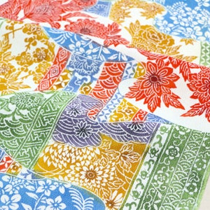 May include: A colourful fabric with a patchwork design featuring various floral patterns, geometric shapes, and traditional Japanese motifs. The fabric is white with red, blue, green, and yellow accents.