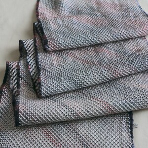 May include: A close-up of a folded fabric scarf with a textured, woven pattern in shades of gray, black, and red.