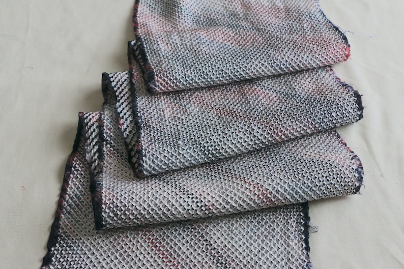 May include: A close-up of a folded fabric scarf with a textured, woven pattern in shades of gray, black, and red.