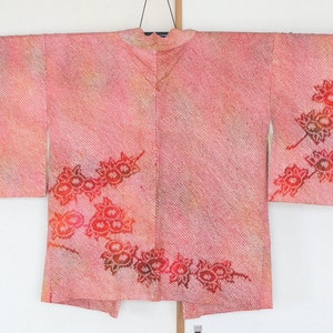 May include: A pink and orange Japanese kimono with a floral pattern. The kimono has a traditional design with a V-neck and long sleeves.
