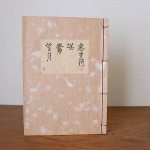 Könnte beinhalten: Ein tannfarbenes Buch mit einem schwarzen Rücken und einem weißen Etikett auf dem vorderen Umschlag. Das Etikett trägt schwarzen Text, der "感書  庵  夢  露" lautet.