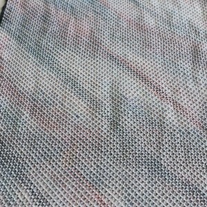 May include: A close-up of a knitted fabric with a diagonal pattern in shades of white, gray, black, and red.