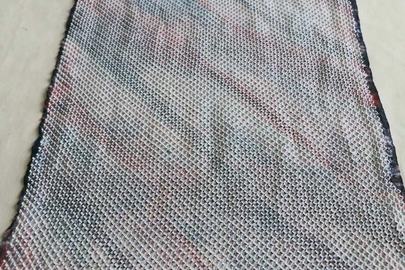 May include: A close-up of a knitted fabric with a diagonal pattern in shades of white, gray, black, and red.