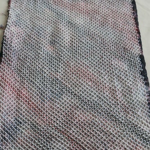 May include: A close-up of a white fabric with a black and red grid pattern. The fabric has a textured, woven appearance.