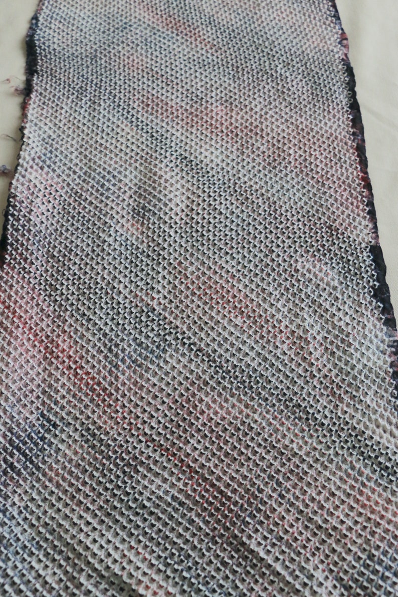 May include: A close-up of a white fabric with a black and red grid pattern. The fabric has a textured, woven appearance.