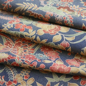 May include: Close-up of a blue fabric with a floral pattern. The fabric features red, yellow, and green flowers, as well as butterflies. The fabric is folded in layers, creating a textured effect.