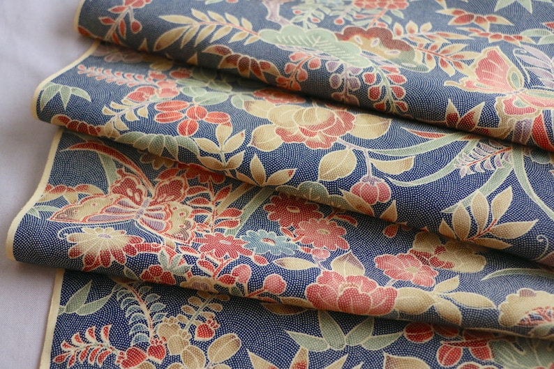 May include: Close-up of a blue fabric with a floral pattern. The fabric features red, yellow, and green flowers, as well as butterflies. The fabric is folded in layers, creating a textured effect.