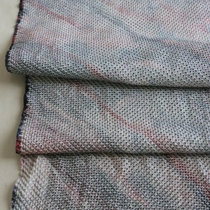 May include: A close-up of a white fabric with a textured pattern of small holes. The fabric has a subtle red and blue striped pattern.