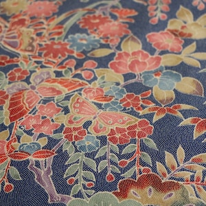 May include: A blue fabric with a floral pattern featuring red, pink, and white flowers, green leaves, and butterflies. The fabric has a textured, almost speckled, appearance.