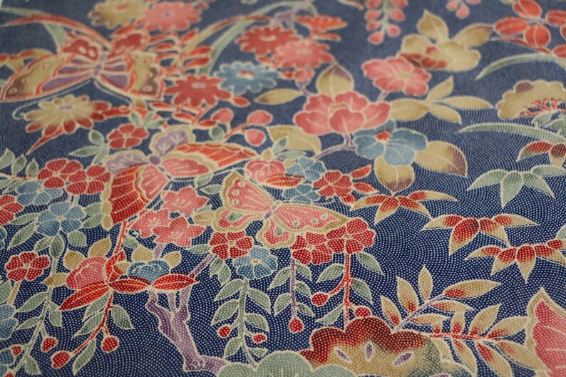 May include: A blue fabric with a floral pattern featuring red, pink, and white flowers, green leaves, and butterflies. The fabric has a textured, almost speckled, appearance.