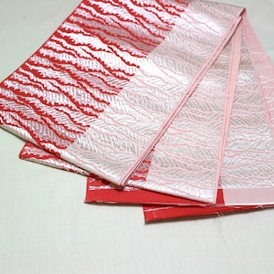 Può includere: Un nastro di tessuto rosso e rosa piegato con un motivo metallico argentato. Il tessuto ha un design ondulato.