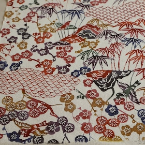 May include: A rectangular piece of paper with a traditional Japanese design. The design features colorful illustrations of flowers, birds, bamboo, and mountains in shades of red, blue, purple, and gold on a white background.