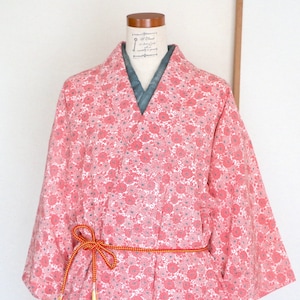 May include: A pink and white floral patterned kimono with a long sleeve and a sash tied around the waist.