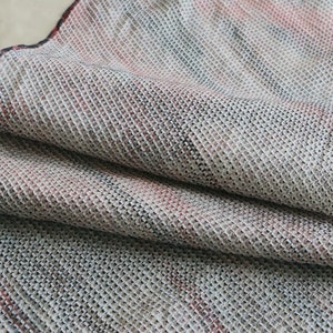 May include: A close-up of a woven fabric with a textured pattern. The fabric is a mix of white, gray, and red.