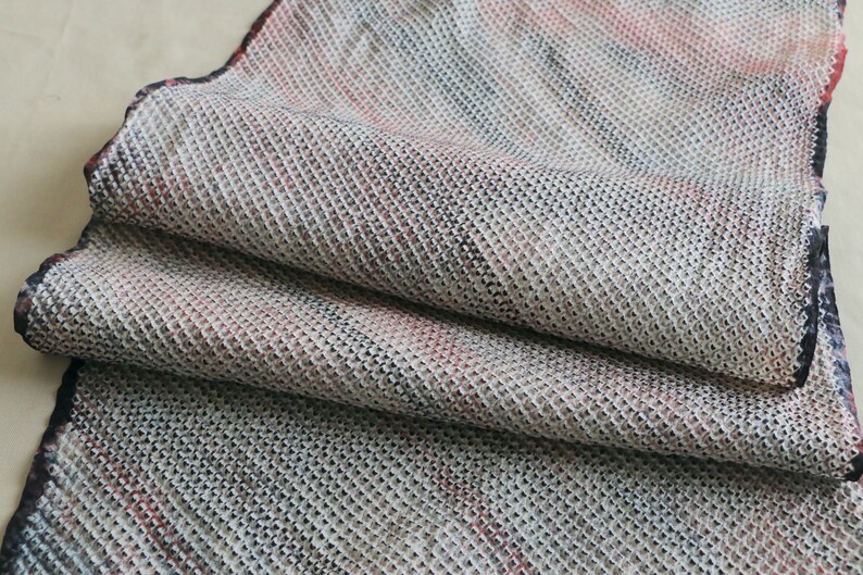 May include: A close-up of a woven fabric with a textured pattern. The fabric is a mix of white, gray, and red.
