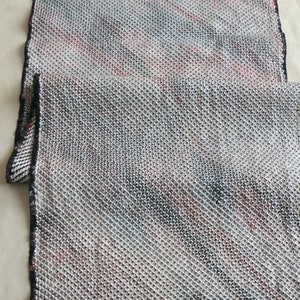 May include: A close-up of a white, black, and red patterned fabric with a textured weave. The fabric has a subtle sheen and a soft, drapey feel.
