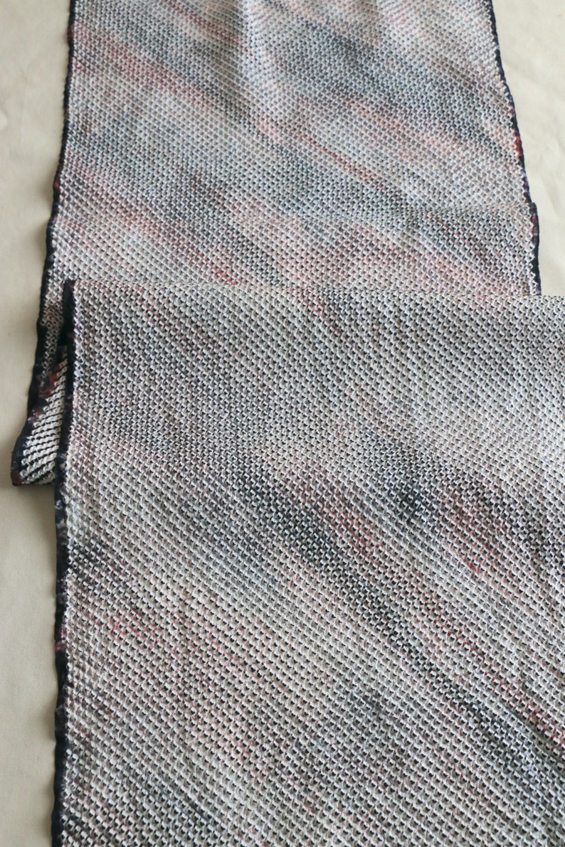 May include: A close-up of a white, black, and red patterned fabric with a textured weave. The fabric has a subtle sheen and a soft, drapey feel.