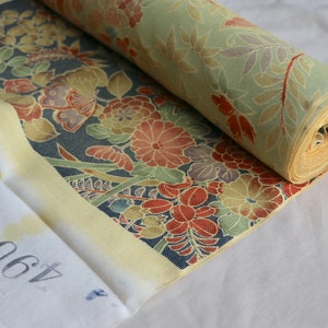 May include: A roll of fabric with a floral pattern in shades of red, yellow, green, and blue. The fabric is rolled up and has a yellow border. The number 460 is written on a white tag.
