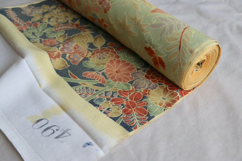 May include: A roll of fabric with a floral pattern in shades of red, yellow, green, and blue. The fabric is rolled up and has a yellow border. The number 460 is written on a white tag.