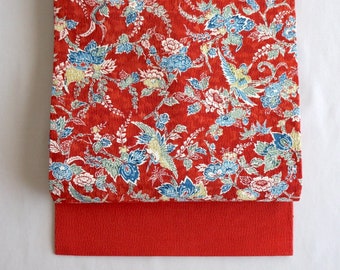 Könnte beinhalten: Roter Stoff mit einem floralen Muster mit blauen und grünen Blumen und Vögeln. Der Stoff ist in der Mitte gefaltet und die untere Hälfte ist einfarbig rot.