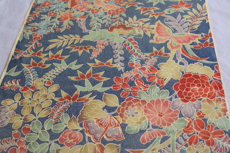 May include: A blue fabric with a repeating pattern of red, yellow, and green flowers and butterflies. The fabric has a textured surface.