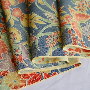 May include: A folded fabric with a blue background and a floral pattern in shades of red, yellow, and green. The fabric has a subtle texture and a delicate, vintage feel.