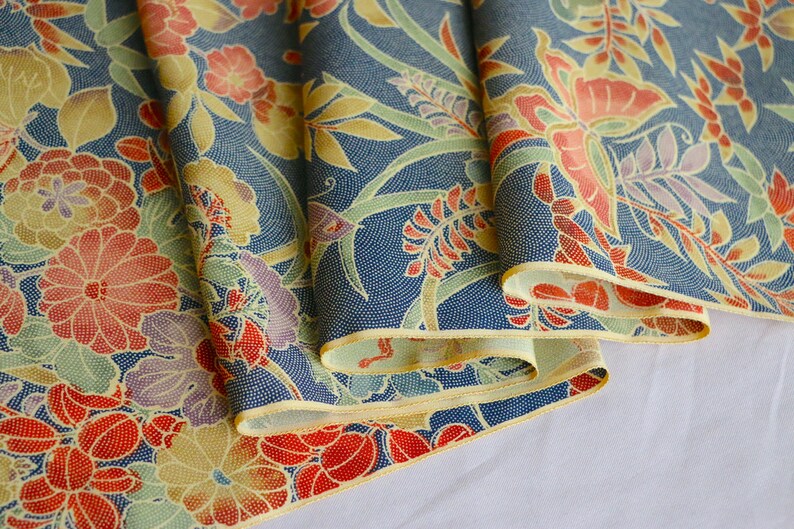 May include: A folded fabric with a blue background and a floral pattern in shades of red, yellow, and green. The fabric has a subtle texture and a delicate, vintage feel.