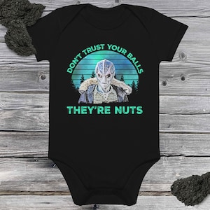 May include: A black short-sleeved baby bodysuit featuring a graphic of an alien wearing a jacket with a fur-lined hood. The design includes a blue and green sunset background with trees and the text: DON'T TRUST YOUR BALLS THEY'RE NUTS.