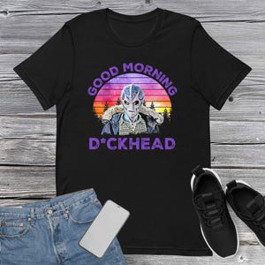 May include: Black t-shirt featuring a retro-style graphic of an alien with a purple "Good Morning D*ckhead" text.