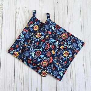 May include: Two navy blue square pot holders with a colorful floral pattern. The pattern includes red, yellow, and blue flowers and leaves. Each pot holder has a small loop for hanging.