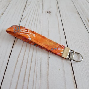 May include: Orange and white patterned fabric key chain with a silver key ring.