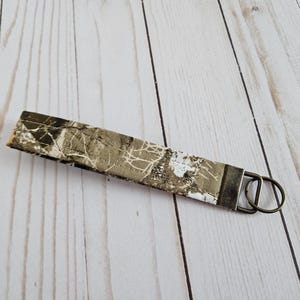 May include: A brown and white camouflage patterned key chain with a bronze metal key ring.