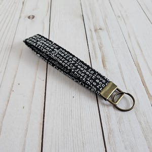 May include: Black and white key chain with a gold metal key ring. The key chain has a repeating pattern of words including "peace", "love", "respect", "equality", "honesty", "truth", and "justice".