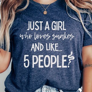 Może przedstawiać: Heather granatowa koszulka z białym napisem "JUST A GIRL who loves snakes AND LIKE... 5 PEOPLE?". Koszulka ma okrągły dekolt i krótkie rękawy. Koszulka jest wykonana z miękkiego, wygodnego materiału.