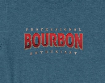 May include: A heathered blue short-sleeve t-shirt featuring the text "PROFESSIONAL BOURBON ENTHUSIAST" printed on the chest. The word "BOURBON" is in large, bold red letters with a dark outline, while the other words are in smaller tan font.