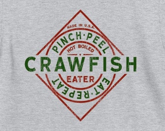 May include: A gray t-shirt with a red and green logo that says "Pinch-Peel Hot Boiled Crawfish Eater Eat Repeat" in a vintage style.