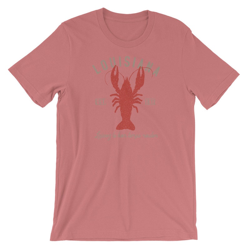 Op de afbeelding: Een roze T-shirt met een vintage-stijl grafische afbeelding van een rode kreeft en de tekst "Louisiana" in groen.
