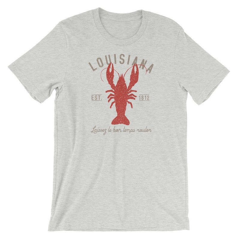 Op de afbeelding: Een grijs T-shirt met een rode kreeft illustratie en de tekst "Louisiana Est. 1812" en "Laissez le bon temps rouler".