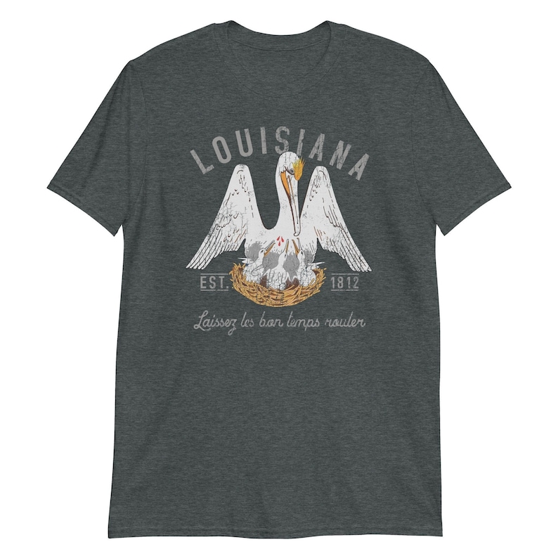 May include: A dark heather gray short-sleeve t-shirt featuring a graphic of a white pelican in a nest with chicks. The text reads LOUISIANA, EST. 1812, and Laissez les bon temps rouler in a distressed white font with orange accents.