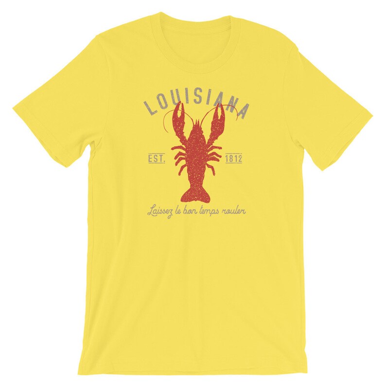 Op de afbeelding: Geel T-shirt met een rode kreeft afbeelding en de tekst "Louisiana Est. 1812" en "Laissez le bon temps rouler".